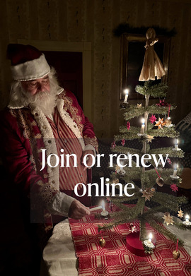 A photo of a living history actor dressed as Santa Claus, lighting candles on a small tabletop Christmas tree