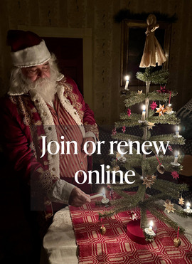 A photo of a living history actor dressed as Santa Claus, lighting candles on a small tabletop Christmas tree