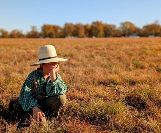 A boy crouches in a field, dressed in Civil War era clothing.