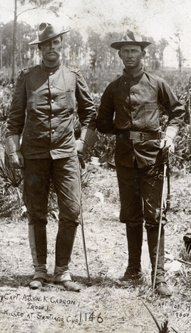 Allyn Capron and Robert H. Bruce, Rough Riders, stand together in uniforms, holding the hilts of their swords in scabbards.