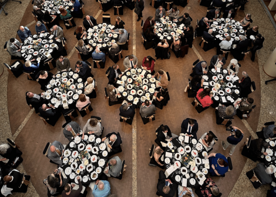 Oklahoma History Center with a third floor view of multiple banquet tables and guests seated. The Winnie Mae replica is suspended overhead.
