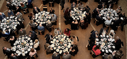 Oklahoma History Center with a third floor view of multiple banquet tables and guests seated. The Winnie Mae replica is suspended overhead.