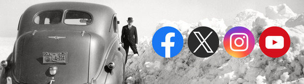 A vehicle parked beside a snow bank that is nearly as tall as the roof of the car. A man stands in the background