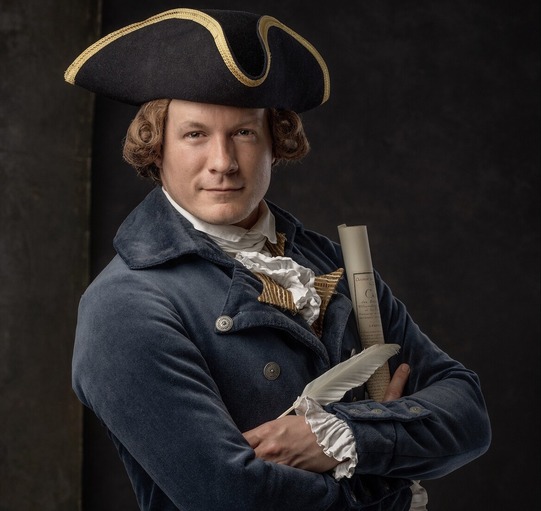 Colonial Williamsburg living historian Kurt Smith wearing Colonial clothing and holding a quill and copy of the Declaration