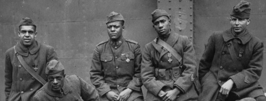 Black World War I soldiers seated together look directly at the camera.