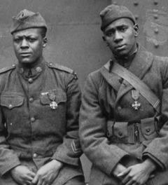 Black World War I soldiers seated together look directly at the camera.