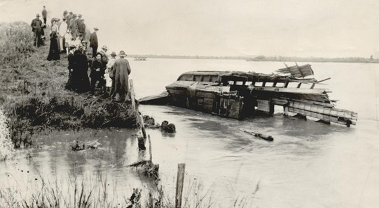 A passenger car of the Rock Island railroad submerged in the Cimarron River after a train accident in 1906. Onlookers stand on a sand bar.