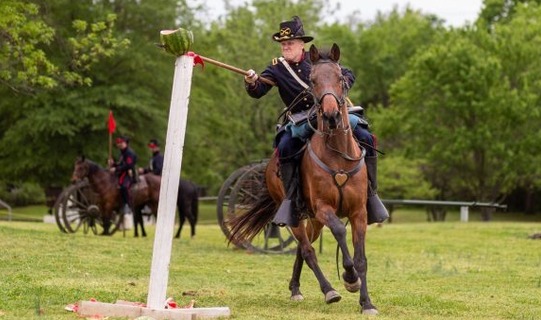 Cody Faber practicing stabbing a watermelon on a pole while riding horseback in uniform.