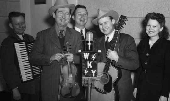 Guitar and fiddle players and others gathered in front of a WKY microphone in the Skirvin WKY studio.