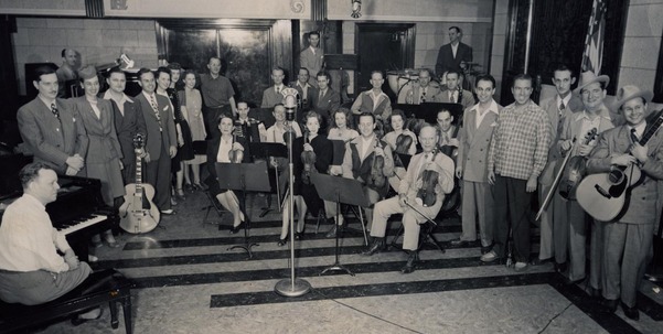 WKY Radio Show players lined up with instruments, surrounding the WKY microphones in the Skirvin Hotel studio.