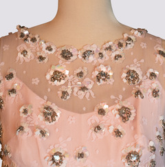 A pink sleeveless ballgown with an overlayment of tulle. Fabric petals of all sizes are sewn with gold sequins at their centers.