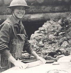 A woman with a hardhat rolling out pie dough near a WWI bunker