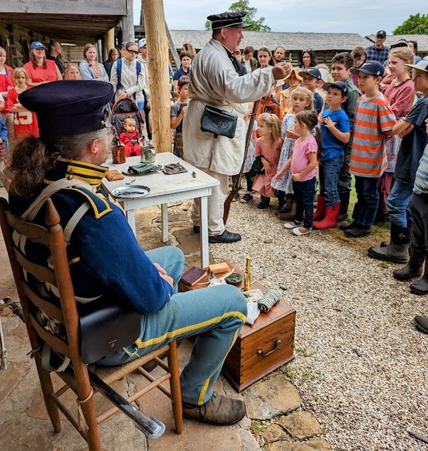 A group of children gather to hear a living history lesson with reenactors at the Fort Gibson stockade. 