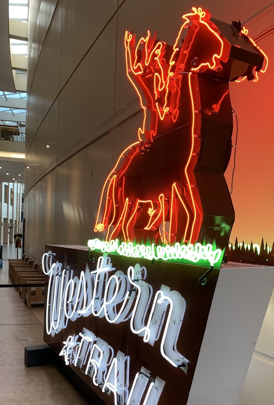 A large neon hotel sign that depicts the shape of a cowboy riding a horse at the top edge of the sign and the words "Western Trail"