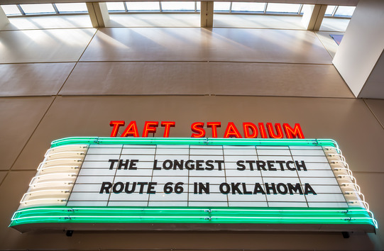 A large neon stadium sign with the words "Taft Stadium" and "The Longest Stretch: Route 66 in Oklahoma" on the marquee.