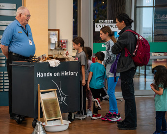 A museum volunteer assists a family of young children and their mother with a Hands-on History cart at the Oklahoma History Center.