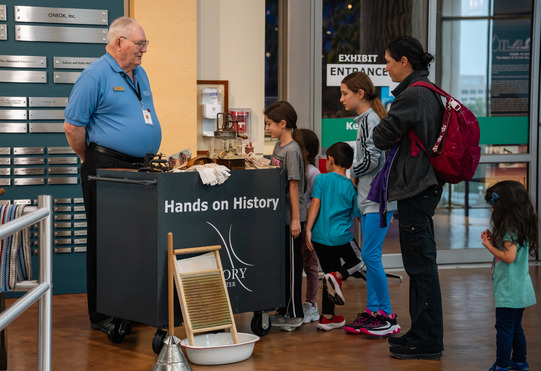 A museum volunteer assists a family of young children and their mother with a Hands-on History cart at the Oklahoma History Center.