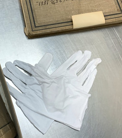 White gloves, an antique book, and other archived files are placed on a museum archives work table.