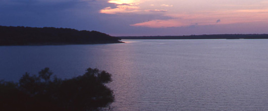 A twilight image of the lake shore of Kaw Lake with clouds obscuring the last light of the day.