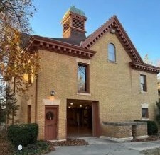 Overholser Carriage House built of wood and buff brick, with a prominent dormer, a cupola with bell roof caps and a large bay entry door.