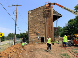 A large cherry picker lift rises two stories to the roofline of the stone Fort Gibson barracks as restoration work takes place