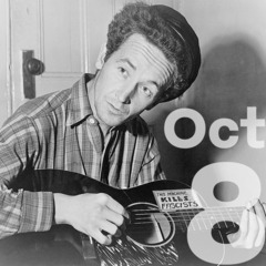 Woody Guthrie leans over a six string guitar that has a sticker that reads 'This machine kills fascists' and the date Oct 8 in large lettering.