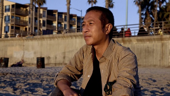 Filmmaker Tony Nguyen looks to the seascape, taking a moment to kneel in the sand of the beach