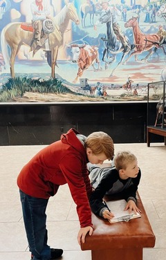 Two boys huddled over a clipboard complete the questionnaire for a scavenger hunt. A mural of Will Rogers can be seen in the background.
