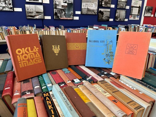 An array of hardback books, some with Oklahoma titles, sitting among many other books stacked on tables.