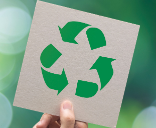 hand holding sheet of cardboard with a green recycle symbol in the middle