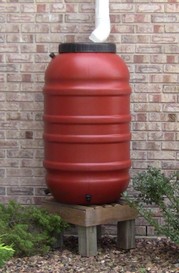 red rain barrel next to a brick wall