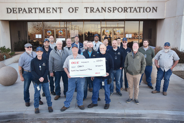 Facilities Management team members stand holding rebate check from OG&E in front of the Department of Transportation building.