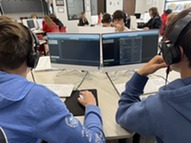 Image of two students sitting at computer participating in coding activities. 