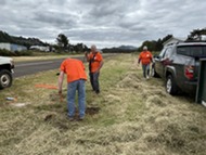 A photo of a group of volunteers at the pacific city airport cleaning up the grass next to the runway.