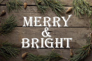 The words Merry & Bright on a wooden background with pine cones and greenery