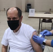 man getting vaccine with black facemask. hands in purple medical gloves administering vaccine. 