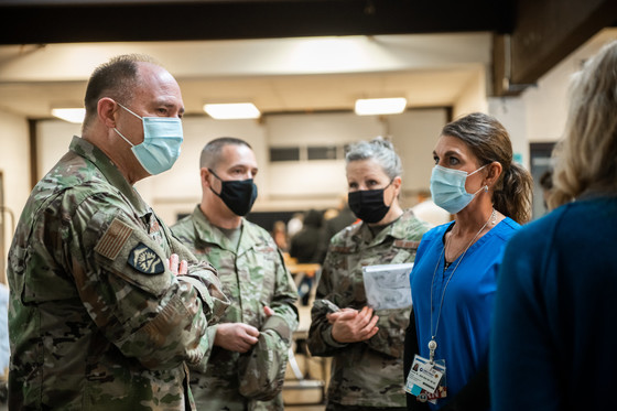 3 people in camo and masks talk with another person in scrubs and a mask. 