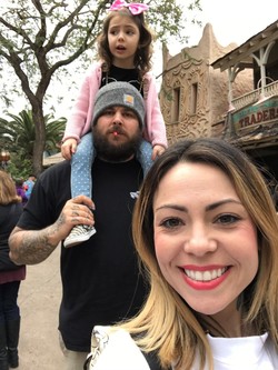 Bearded man with beanie on carries child on shoulders, while woman takes selfie