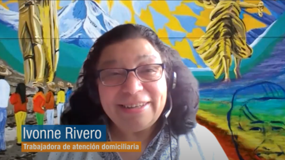 Video screeenshot of woman with microphone on in front of colorful artwork. 