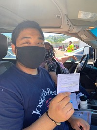 boy in blue shirt with black mask holds vaccination card