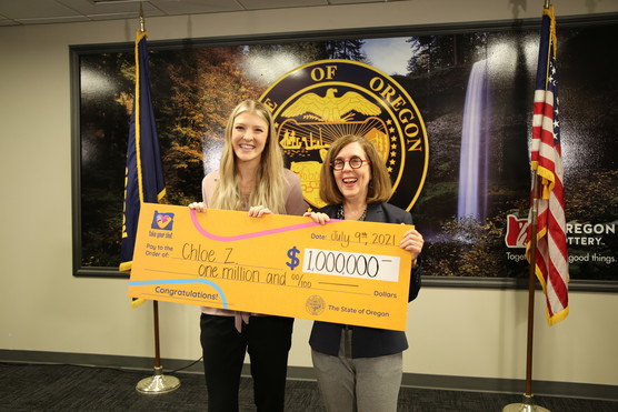 Two women hold very large 1 million dollar check in front of them and smile at the camera. 