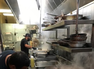 Two people work in a stainless-steel kitchen with steam rising from the grills.