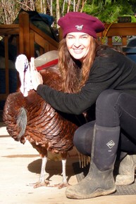 Kneeling woman wearing red beret smiles and holds onto a turkey. 
