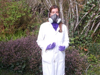 Woman wears long white jacket, gas mask and purple gloves. 