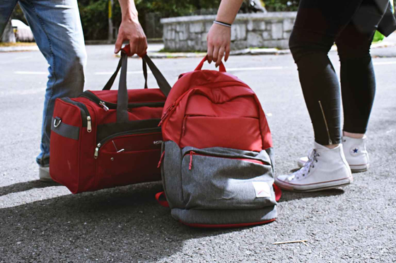 Photograph shows two people picking up a duffle bag and backpack heading home from college for winter break. 