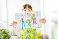 a young girl holds up a picture with a drawing of a family
