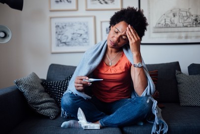 Image: a woman sits on a couch with her hand on her forehead