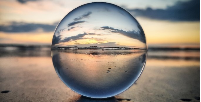 A glass crystal ball on the beach that magnifies the sunset behind it. 