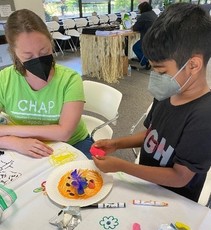Image shows a masked child playing with clay next to a masked CHAP volunteer.