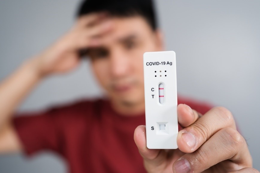 A man holds up a positive COVID-19 test